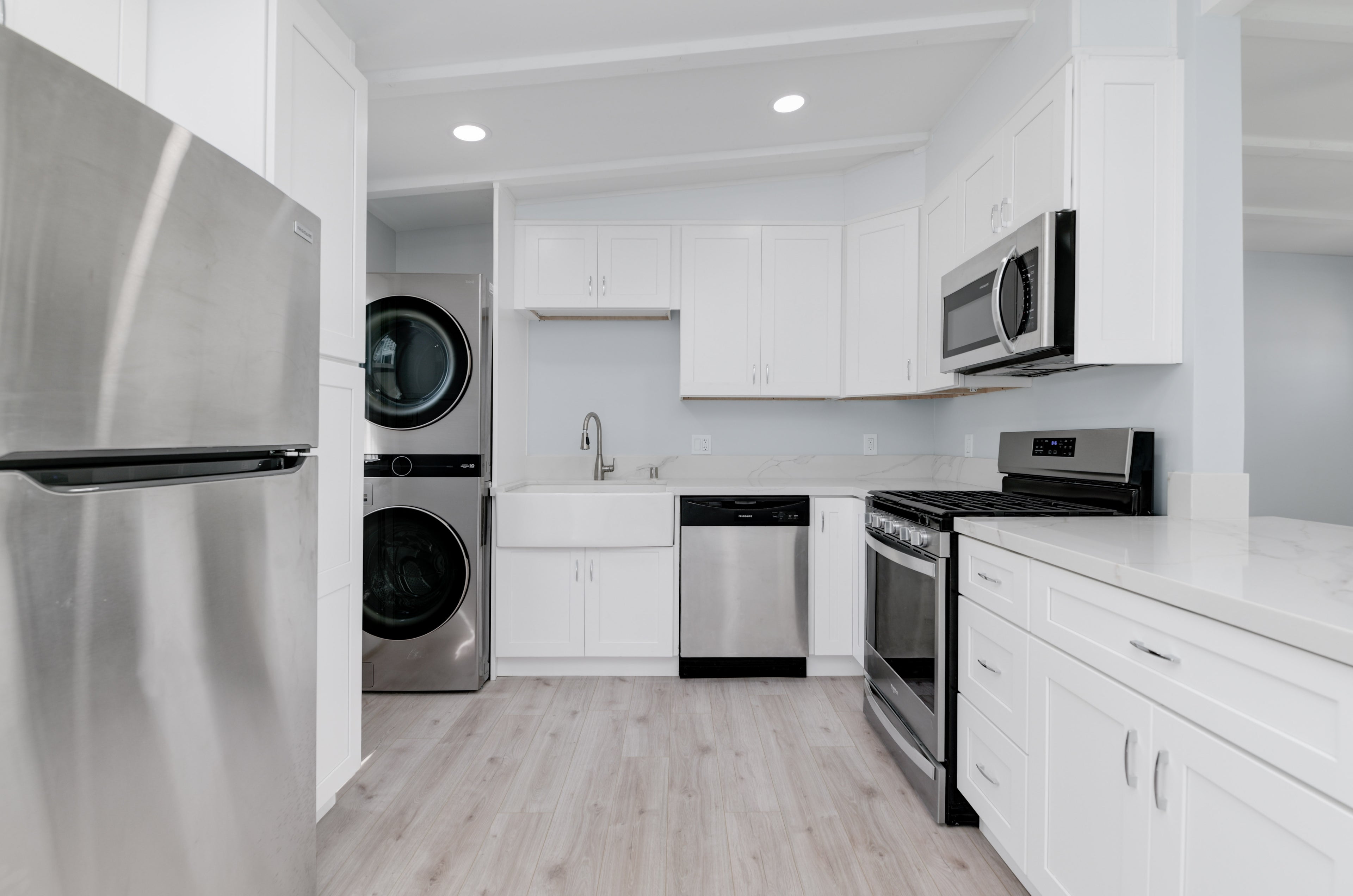 White and grey modern kitchen with stacked washer and dryer, stainless steel finishes, and sleek marble surfaces – Kitchen Remodel and Home Remodeling San Diego project. Remodeling Source of San Diego