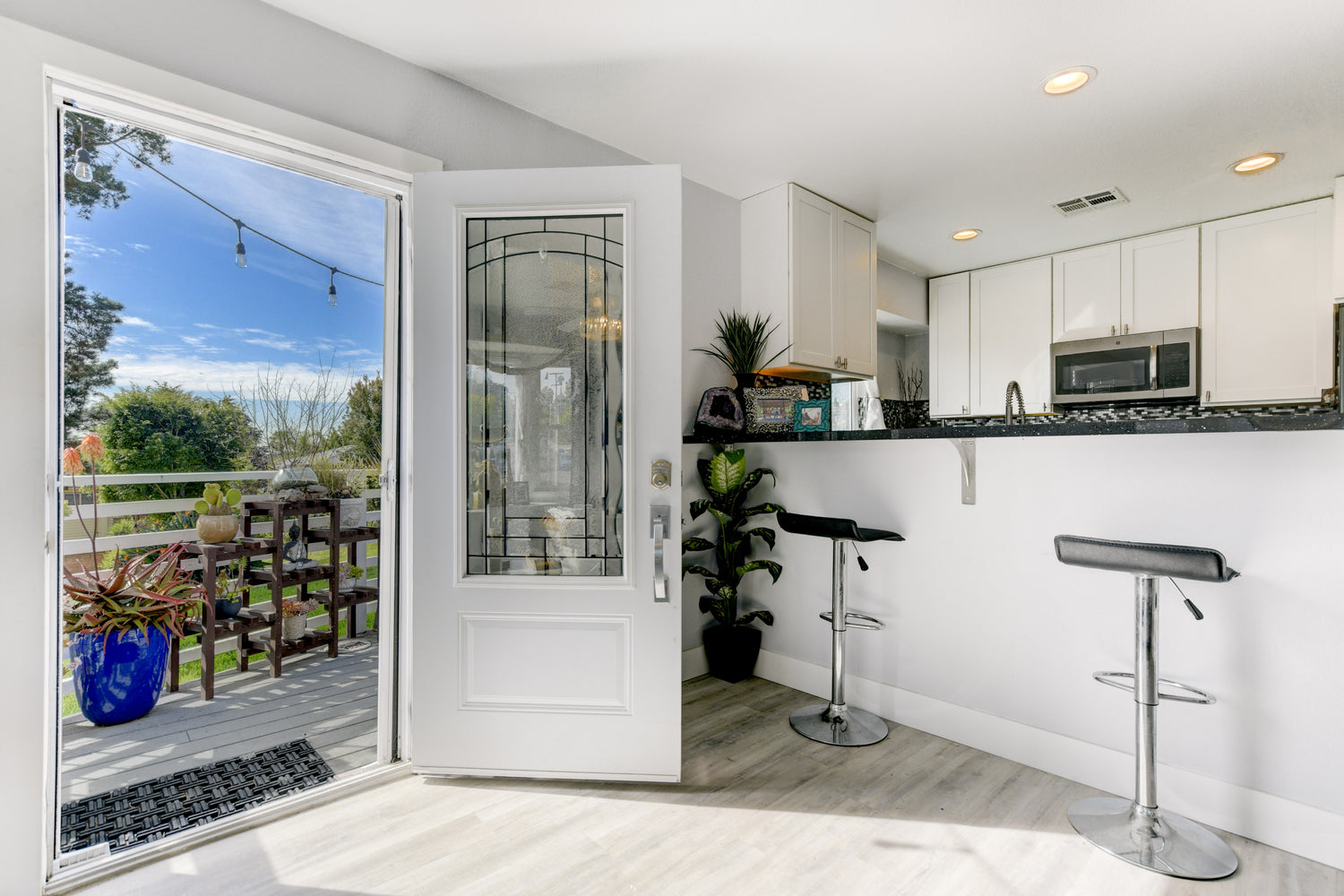 Home entryway with white door featuring elegant glass panel, modern lock system, grey flooring, and view into remodeled kitchen and bar – Home Remodeling San Diego. Remodeling Source of San Diego.