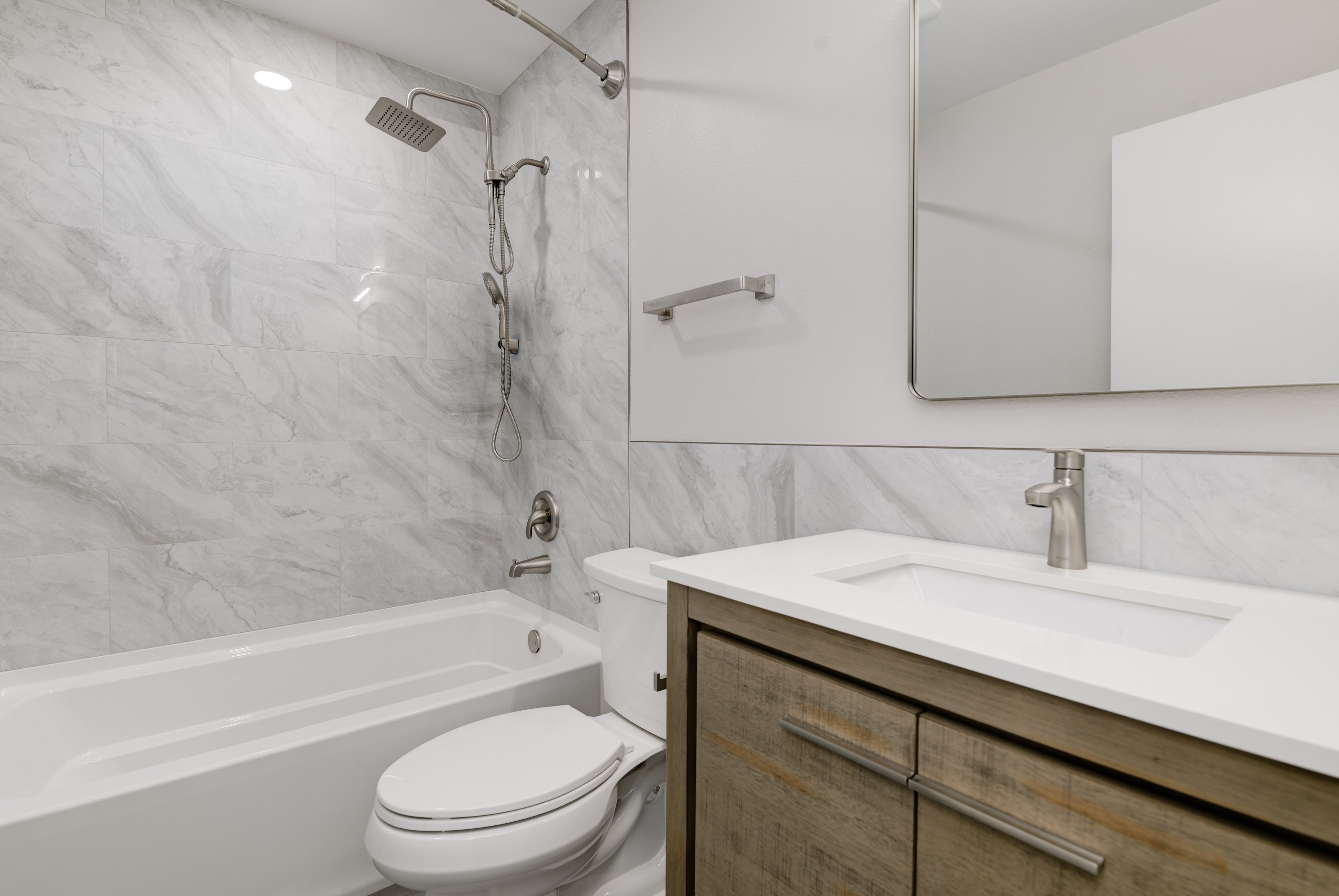 Modern bathroom with white marble walls, wooden vanity, and glass shower enclosure. Remodeling Source of San Diego. Go RSSD.