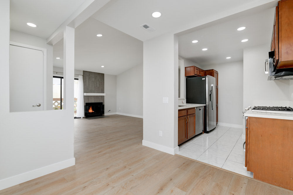 Modern kitchen with wooden cabinets and stainless steel appliances in a well-lit room. Living room with modern fireplace, grey tiles. White tile. Remodeling Source of San Diego. Go RSSD.
